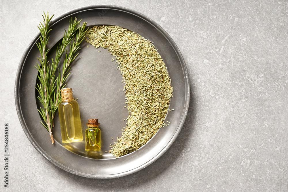 Tray with fresh and dry rosemary and oil on grey table