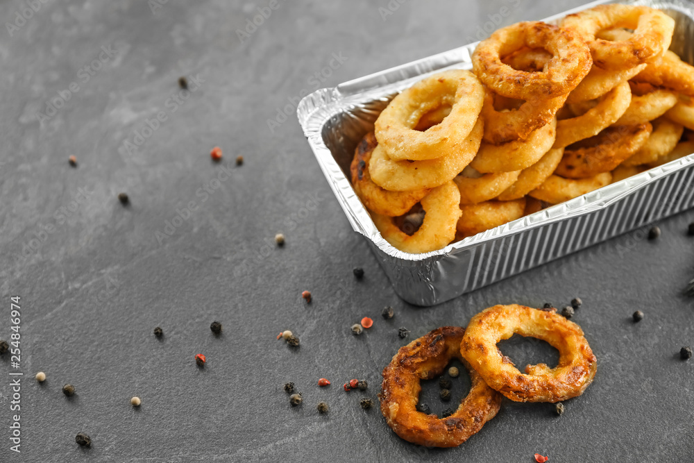 Takeaway box with tasty onion rings on grey table