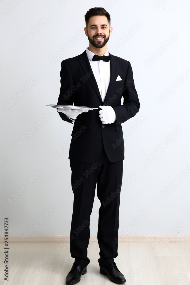 Waiter with empty tray near light wall