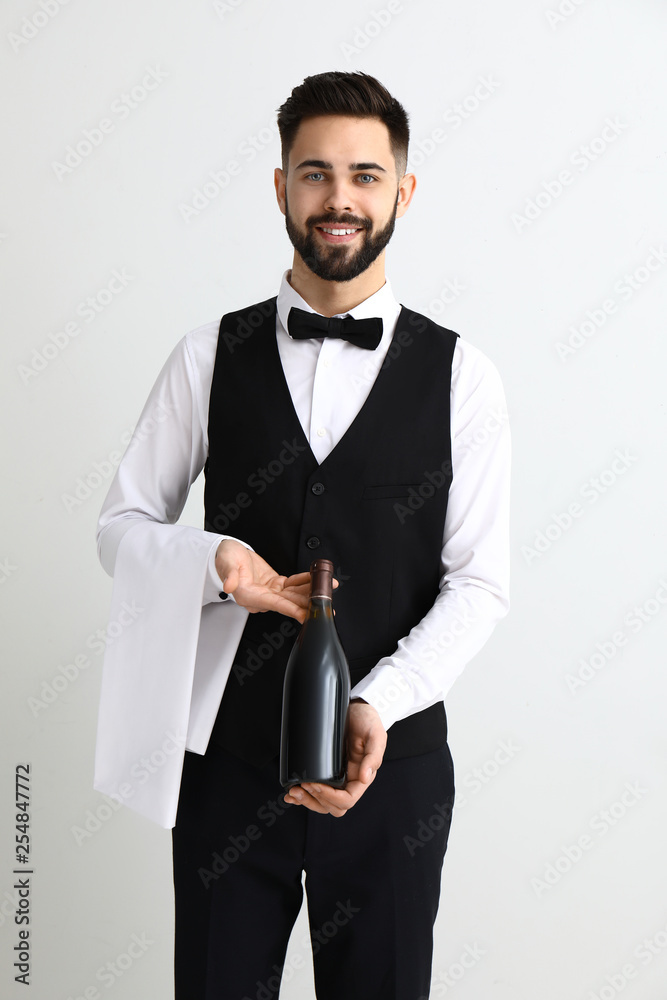 Handsome waiter with bottle of wine on light background