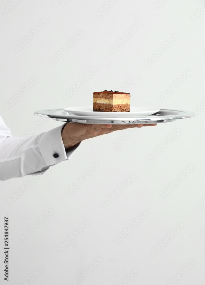 Hand of waiter with tasty dessert on light background