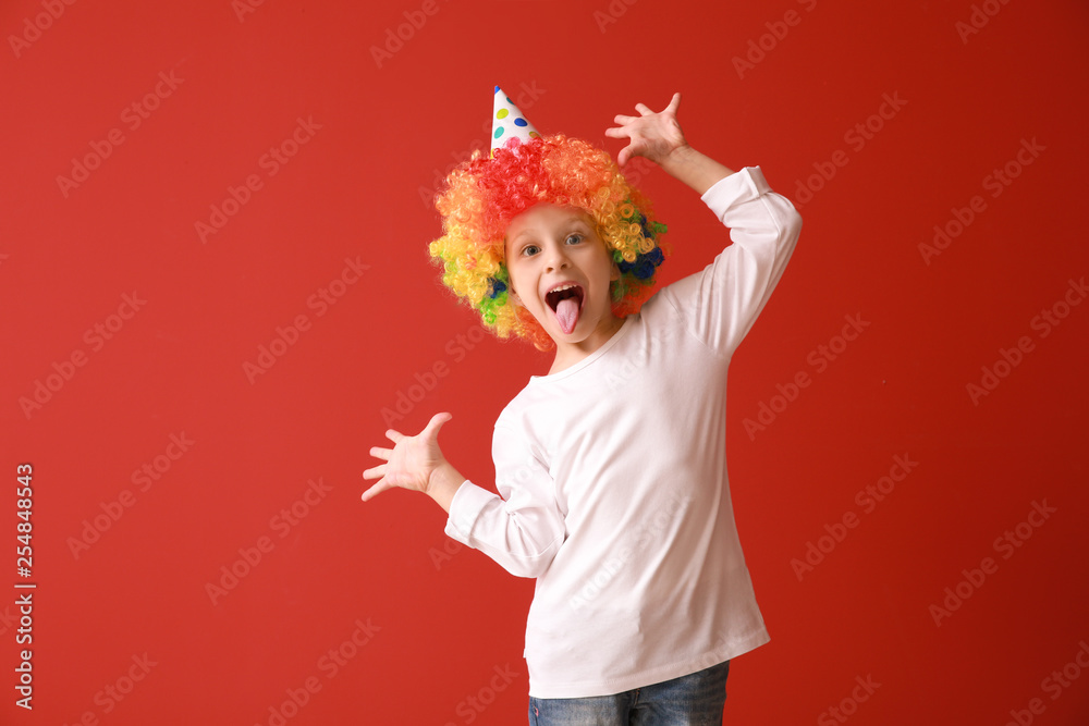 Funny little girl in bright wig on color background. April fools day celebration