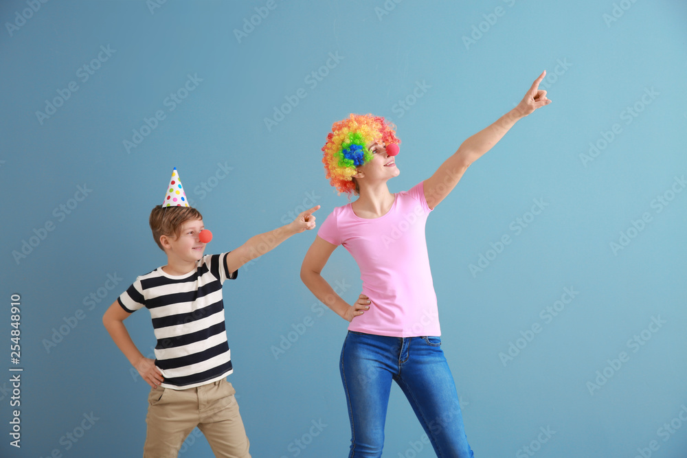 Little boy and his mother in funny disguise on color background. April fools day celebration