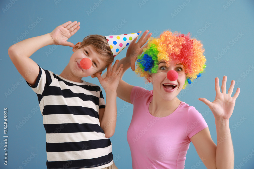 Little boy and his mother in funny disguise on color background. April fools day celebration