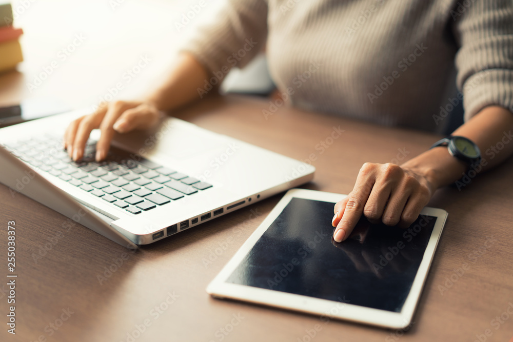 Woman using laptop and digital tablet during working in office, hands close up.