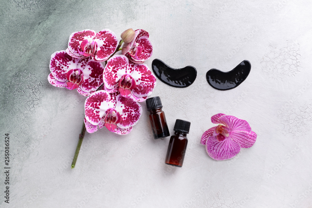 Under-eye patches with essential oil and orchid flowers on light background