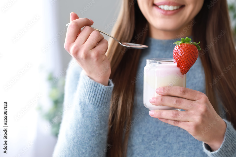 Young woman eating tasty yogurt at home, closeup