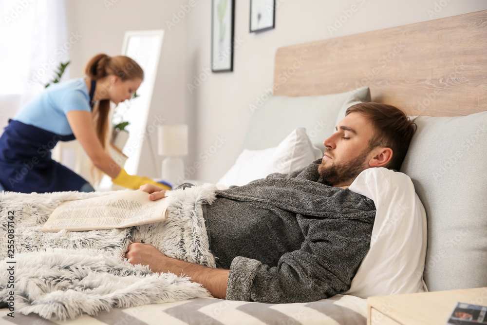 Lazy husband lying in bed while his wife doing chores at home