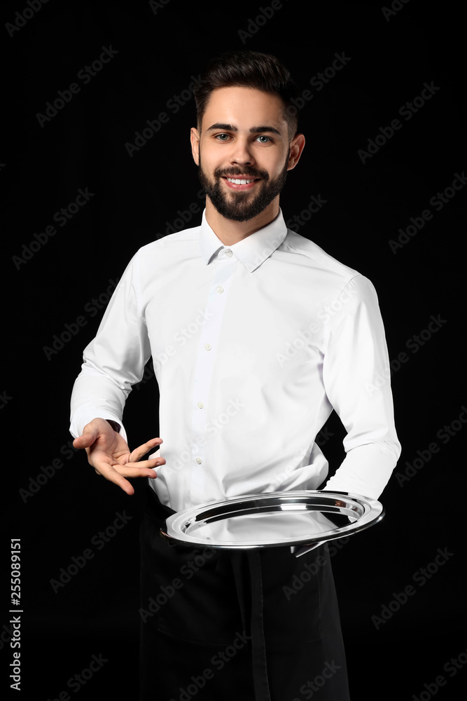 Handsome waiter with empty tray on dark background