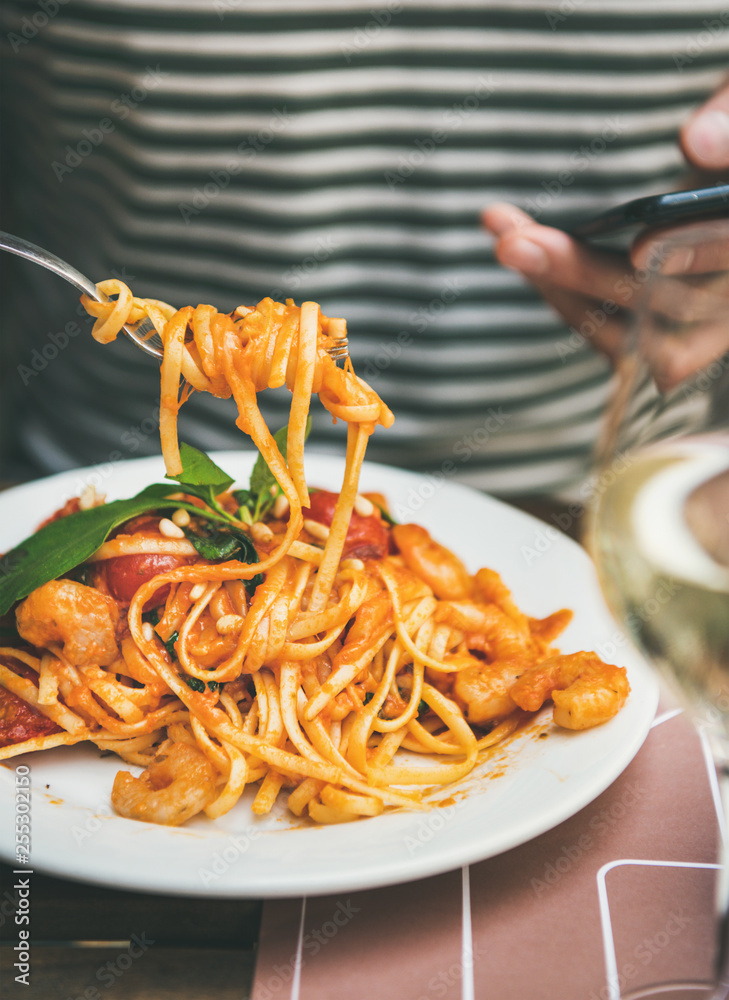 Italian dinner at bistrot with spaghetti pasta with shrimps and glass of white wine. Man eating past