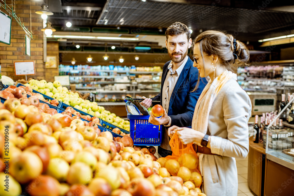 Young and beautiful couple choosing fresh apples while buying food in the supermarket