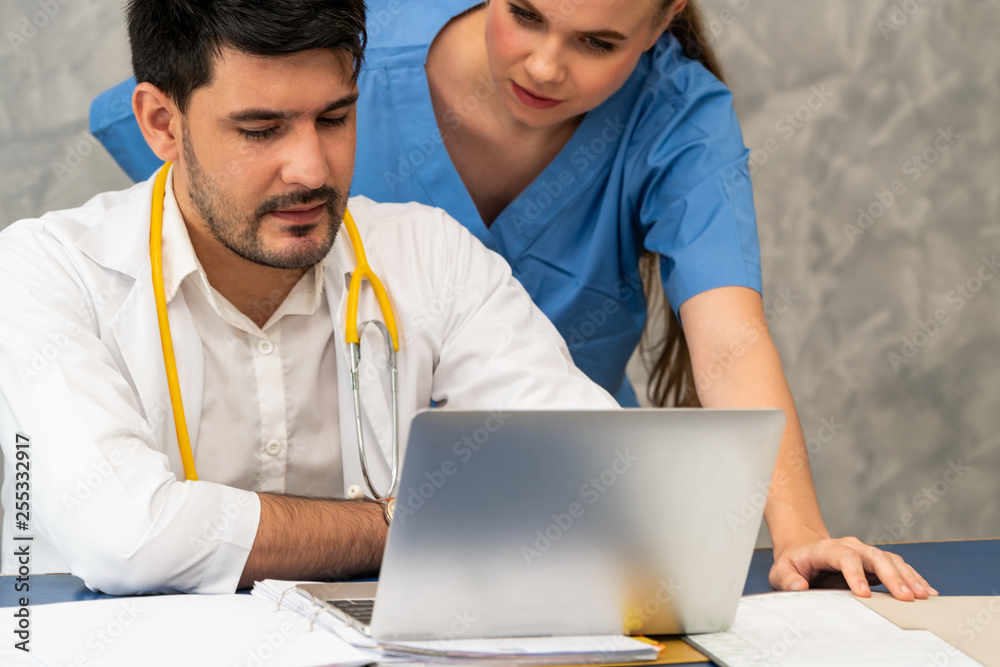 Happy doctor and nurse working with laptop computer in hospital office. Healthcare and medical conce