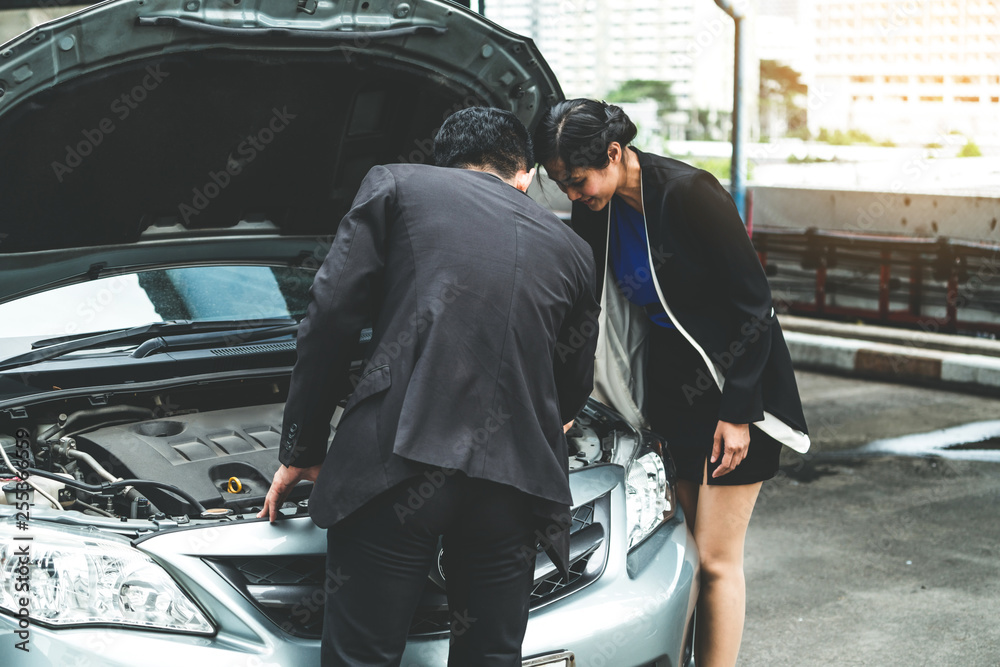 Man help woman fix the car problem. He pop up the car hood to repair the damaged part.