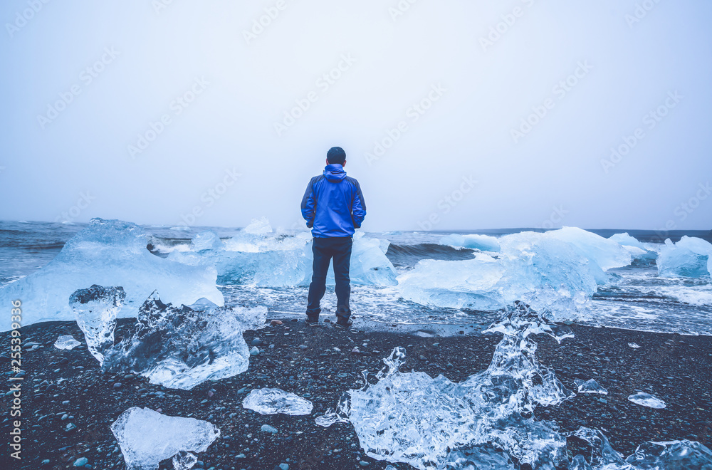 年轻人旅行者前往冰岛钻石海滩。黑沙滩上的冰冻冰流着fr