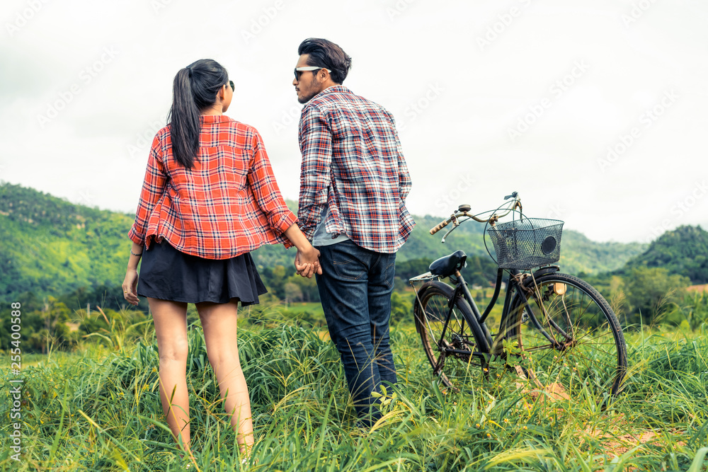 Happy young couple of man and woman ride bicycle at green grass field on the hills. Love and travel 