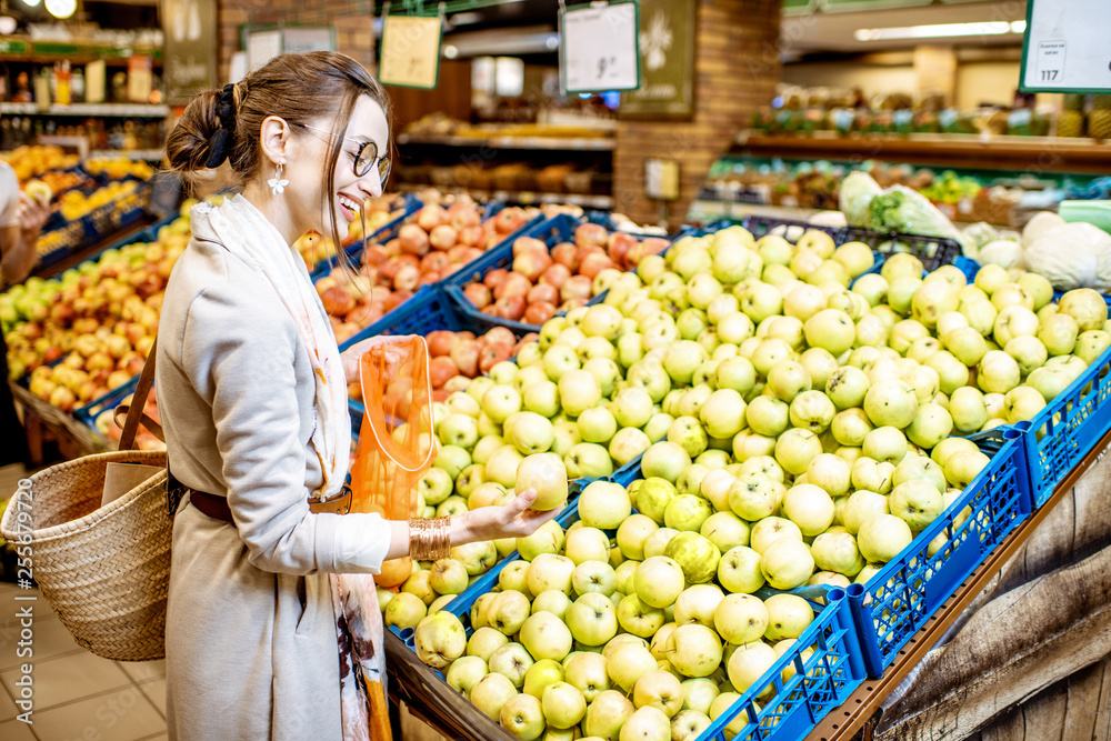 Young woman choosing apples to buy standing in the department with fruits and vegetables in the supe