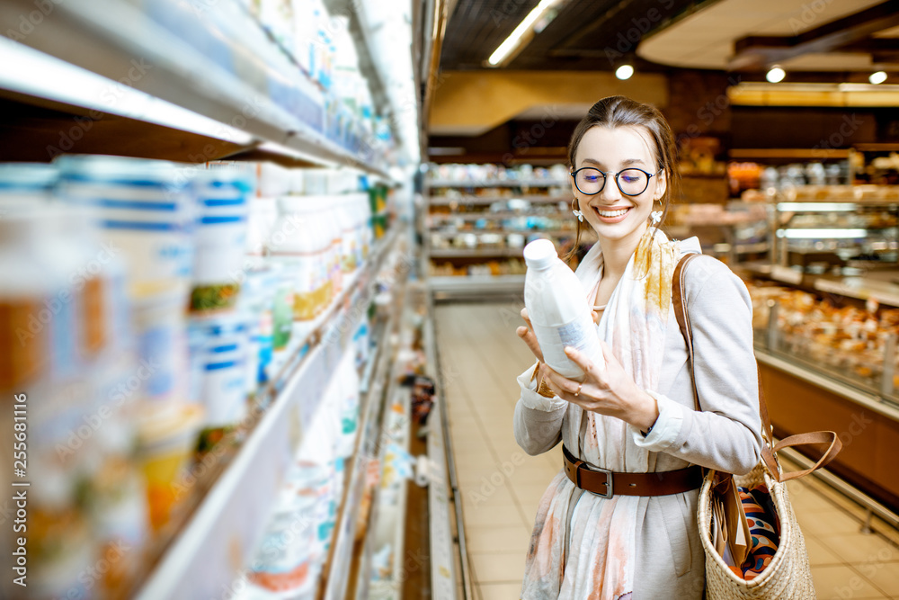 年轻女子站在超市里摆放乳制品的货架旁挑选牛奶