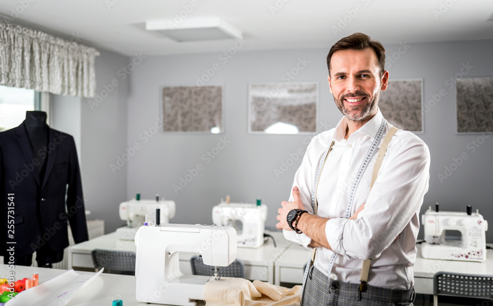 Smiling tailor shop owner standing above workshop desk, fashion design business