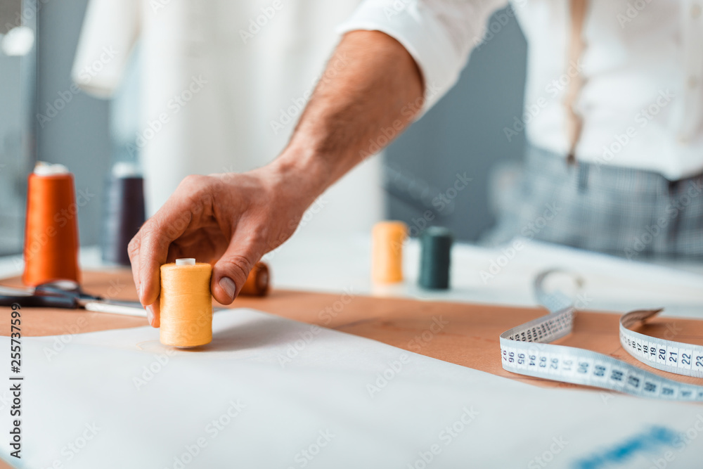 Professional tailor holding sewing thread during work at fashion design workshop