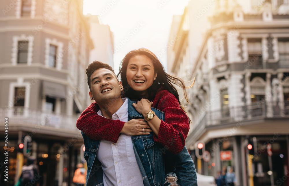 Asian couple piggybacking on city street