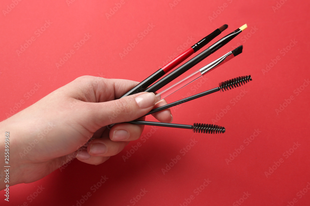 Female hand with tools for eyebrows correction on color background