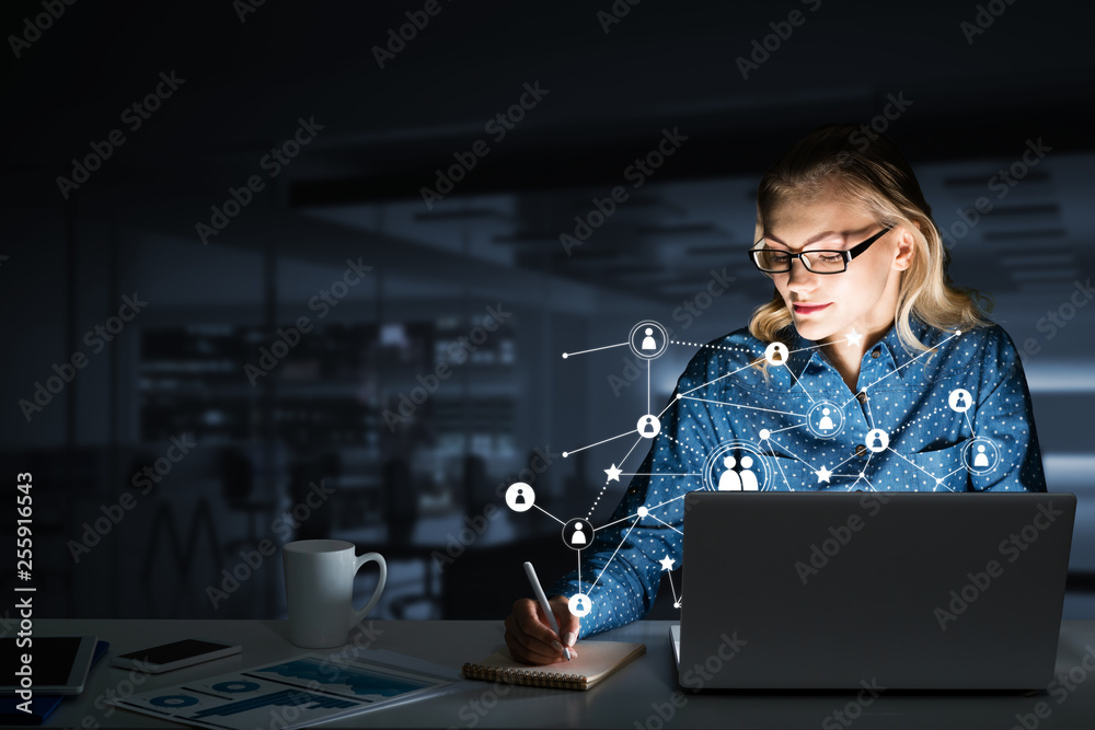 Attractive blonde wearing glasses in dark office using laptop. Mixed media