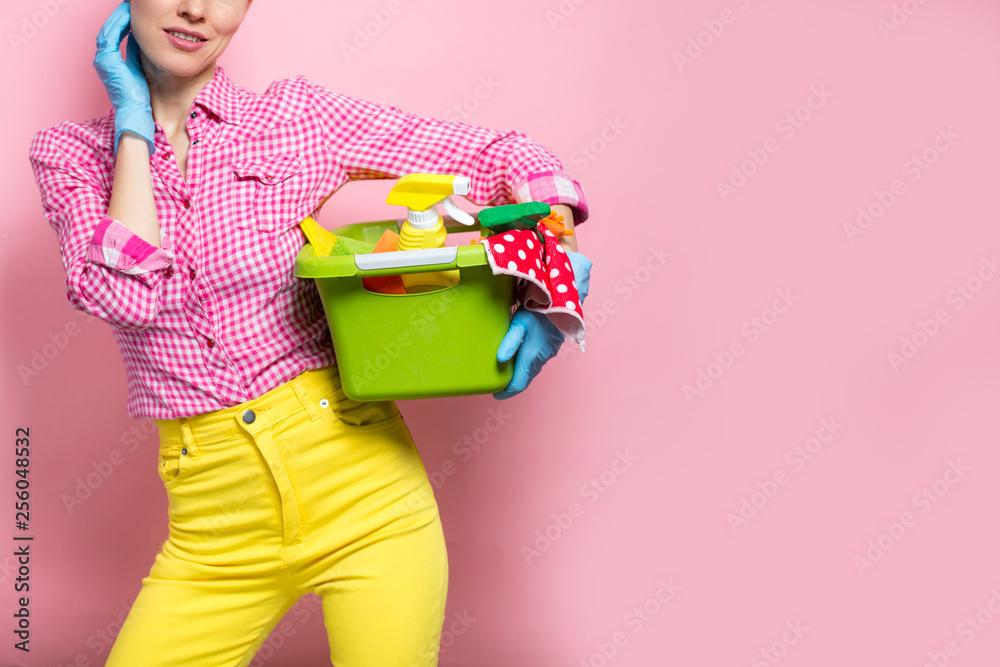 Young woman in rubber gloves holding bucket with cleaning supplies