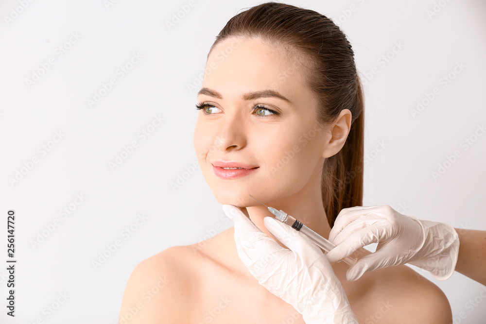 Young woman receiving injection in face on light background