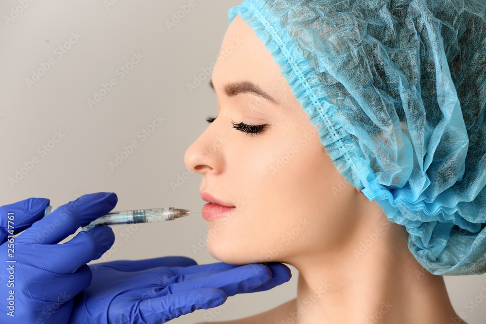 Young woman receiving injection in face on light background