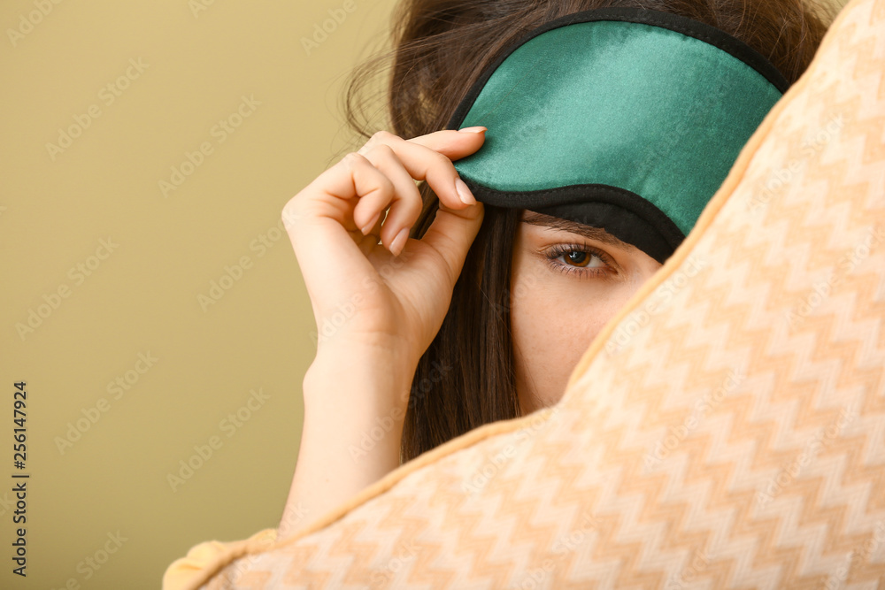 Sleepy young woman with mask and pillow on color background