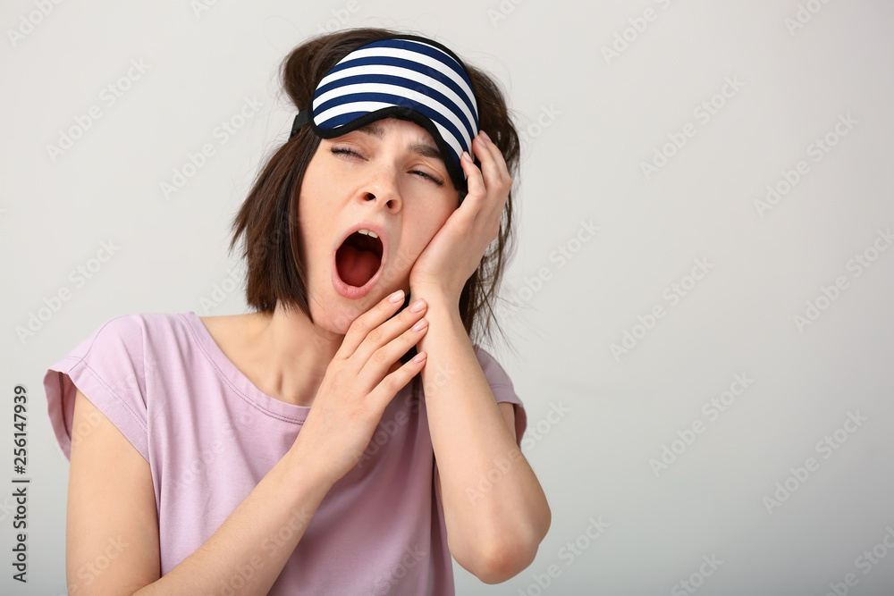 Sleepy young woman with mask on light background