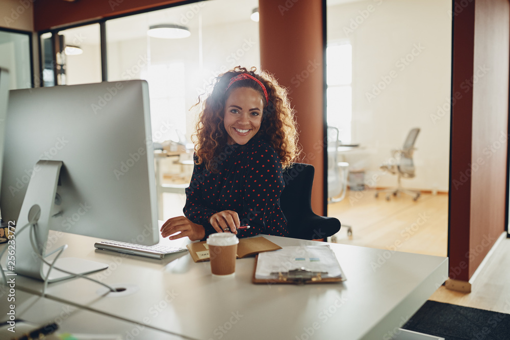 Smiling businesswoman sitting at her workstation in a large offi