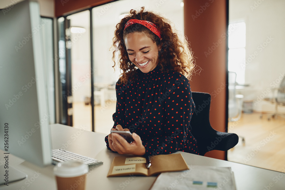 Laughing young businesswoman using a cellphone at her office des