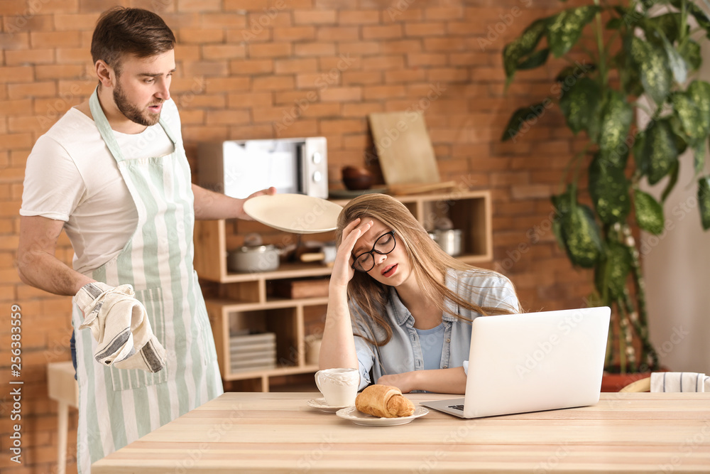 Tired wife working while her indignant husband doing chores at home