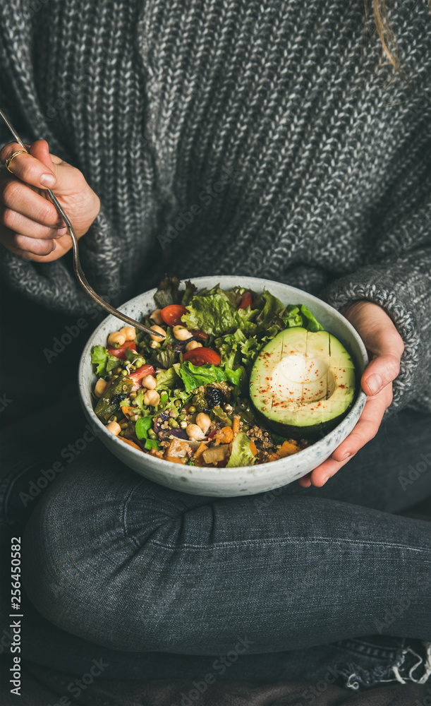 健康的素食晚餐。穿着牛仔裤和保暖羊毛衫的女人拿着碗，里面有新鲜的沙拉，avo