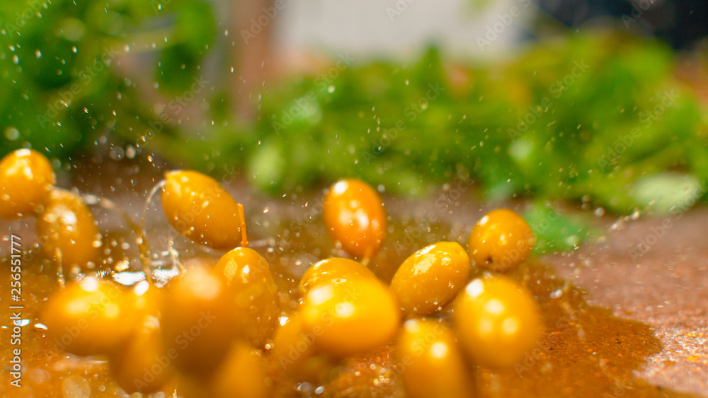 MACRO Ripe olives fall into a puddle of olive oil and splash it over the table.