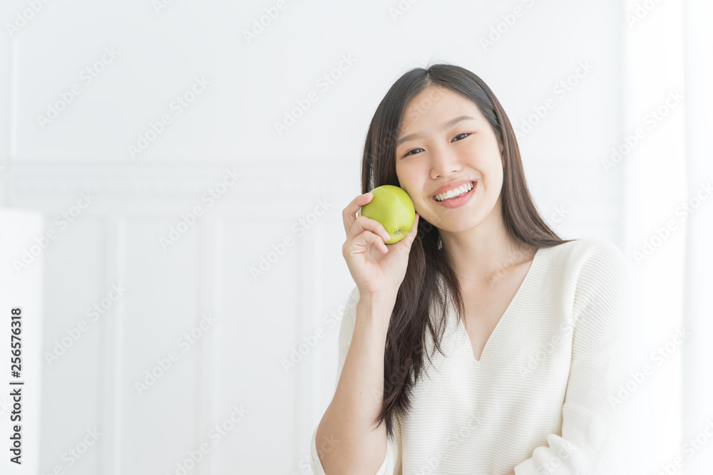 Young Asian woman showing green apple, indoors portrait