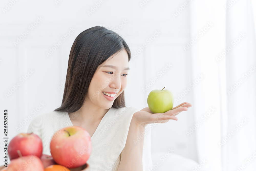 Young Asian woman showing green apple and red apple, indoors portrait