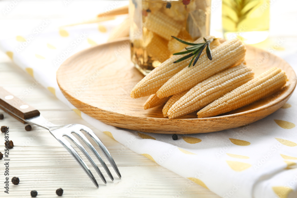 Plate with canned baby corn cobs on wooden table