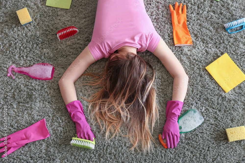 Tired housewife with cleaning supplies lying on soft carpet