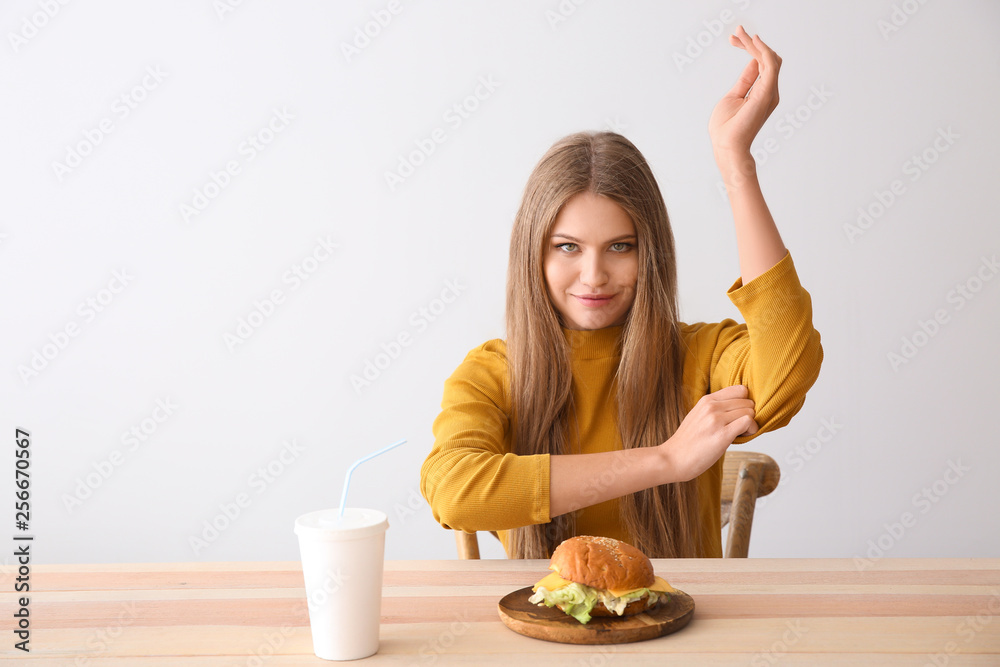 Young woman with tasty burger and soda at table