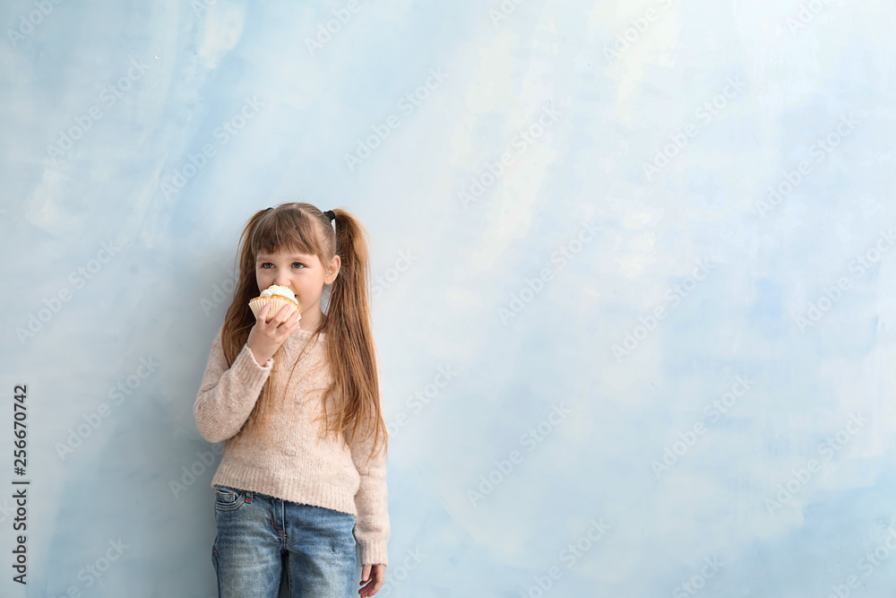 Funny little girl eating tasty cake on color background