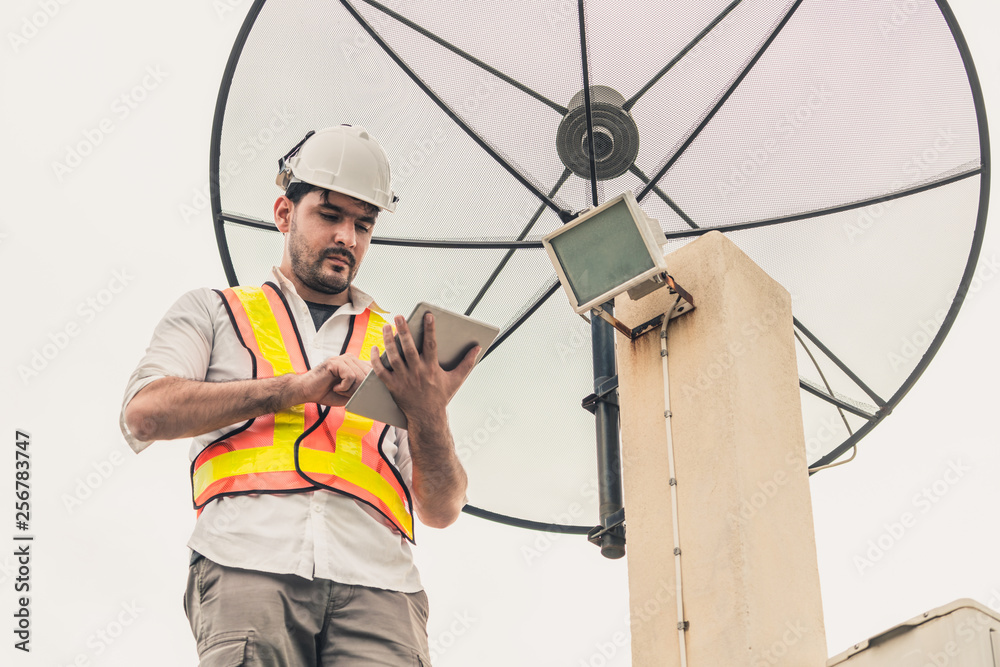 Professional technician or engineer standing on roof top of building working with satellite dish. Co