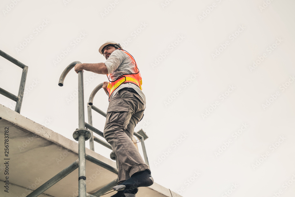 年轻的建筑工人或工程师在建筑物顶部爬梯子。工程项目混凝土