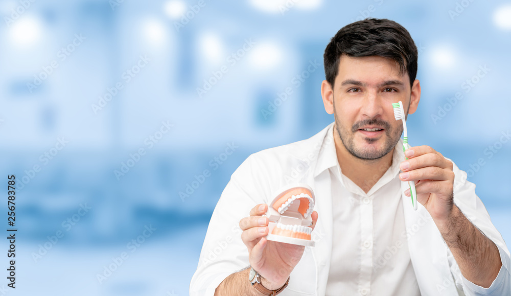 Young male dentist showing toothbrush and denture in dental clinic. Selective focus at the toothbrus