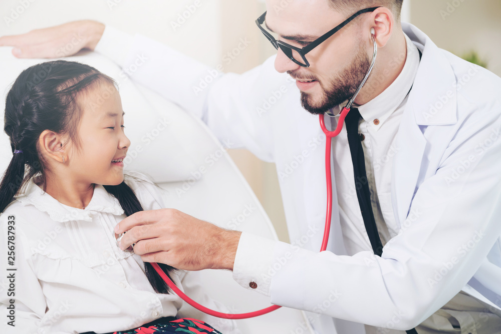 Young male doctor examining little kid in hospital office. The kid is happy and not afraid of the do