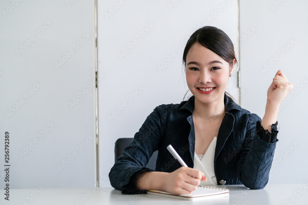 一位年轻漂亮的亚洲美女坐在办公桌旁在笔记本上写信。内容作家a