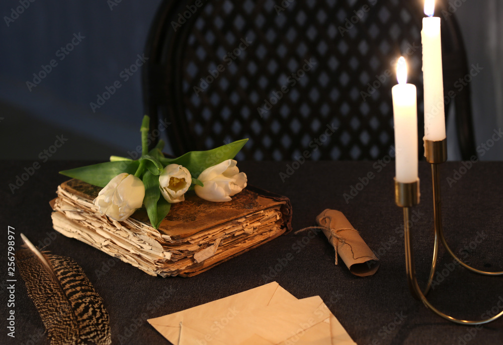 Burning candles with old book and flowers on table