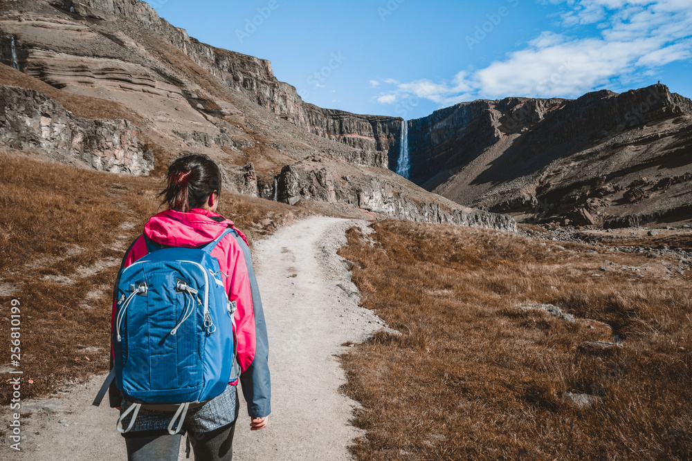 Woman traveler trekking in Icelandic summer landscape at the Hengifoss waterfall in Iceland. The wat