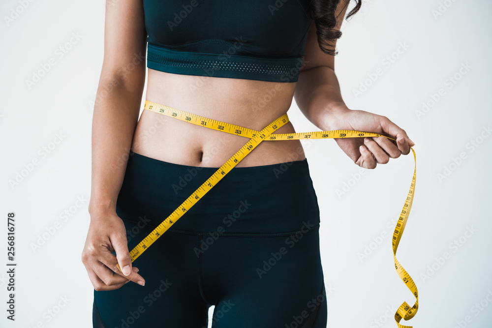 Close up shot of woman with slim body measuring her waistline and torso. Healthy nutrition and weigh